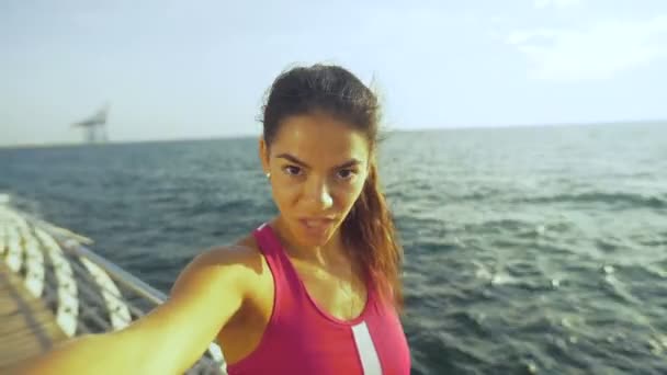 Söt ung brunett flicka tar selfies och vilar på trä strandpromenaden efter morgon jogging. — Stockvideo