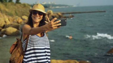 Sevimli gülümseyen kadın selfies, mavi sakin deniz kenarında taş kalırken alarak tabaklanmış.