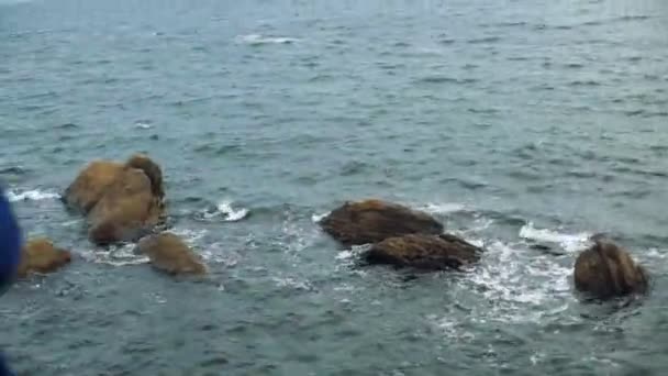 Deux jeunes gens heureux debout sur la pierre et regardant les vagues faites par un vent violent . — Video