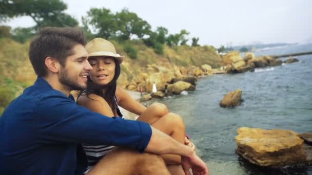 Young funny smiling woman talking different stories and her husband listening to her, while sitting on the beach. — Stock Video