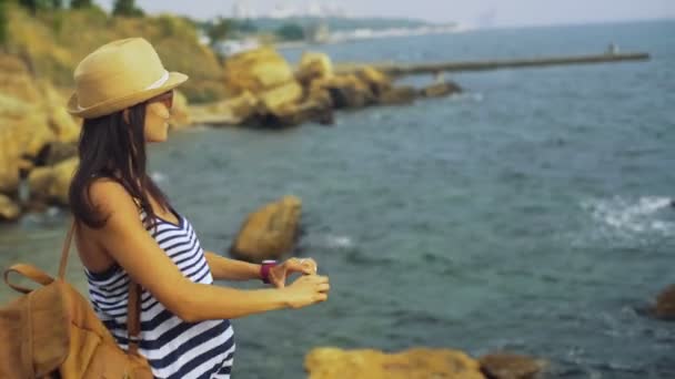 Attraktiv ung garvade lugna leende damen tar selfies, medan du bor på stenen nära blå havet. — Stockvideo