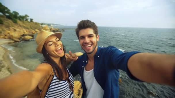 Guapo joven sonriente hombre besando a su novia, mientras posando en una foto selfie, quedarse en la playa . — Vídeos de Stock