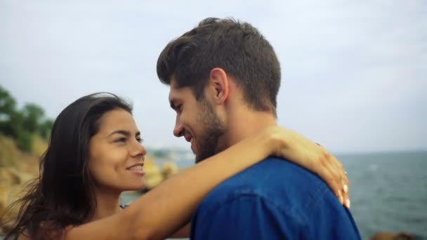 Glückliches lächelndes Paar, das sagt, wie sehr es sich liebt, während es an einem schönen steinigen Strand steht. — Stockvideo