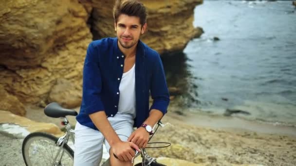 Jeune beau modèle souriant posant sur une plage avec un vélo de vitesse . — Video