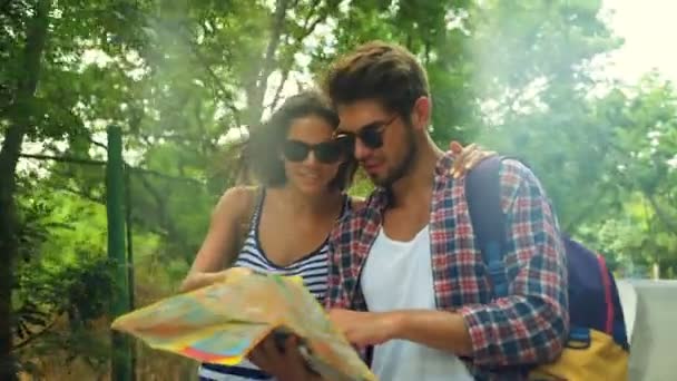 Adorável jovem casal sorrindo segurando um mapa nas mãos, andando em um parque verde . — Vídeo de Stock