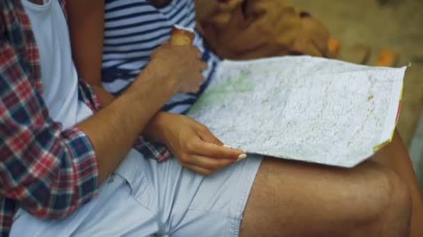 Close up de dois jovens sentados em um banco com um mapa e sorvete nas mãos . — Vídeo de Stock