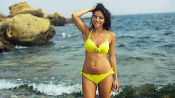 Krásná štíhlá opálená brunetka pózuje na stylové žluté plavání oblek na pláži. — Stock video