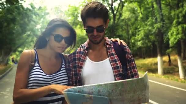 Zwei lächelnde Menschen, die mit einer Landkarte durch den schönen grünen Park spazieren. — Stockvideo