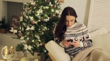 mutlu genç kadın Noel ağacının yanında SMS yazma
