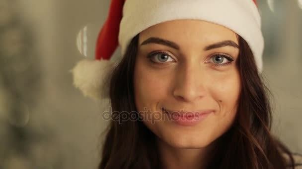 Закройте женщину в портрете в шляпе Санты, позируя на фоне огней деревьев. , рождественский праздник концепции, счастья и эмоций — стоковое видео
