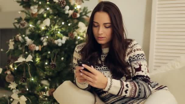 Gelukkig jonge vrouw schrijven sms in de buurt van de kerstboom — Stockvideo