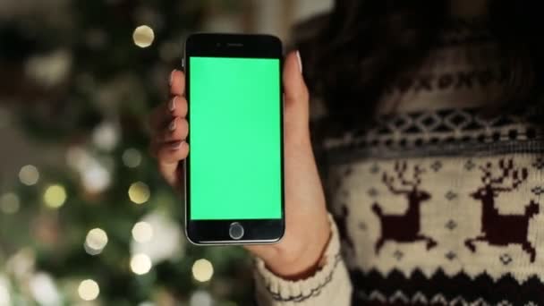 Gros plan des mains féminines touchant le smartphone. Écran vert Chroma Key. Ferme là. Suivi du mouvement. avec fond flou décoration de Noël 