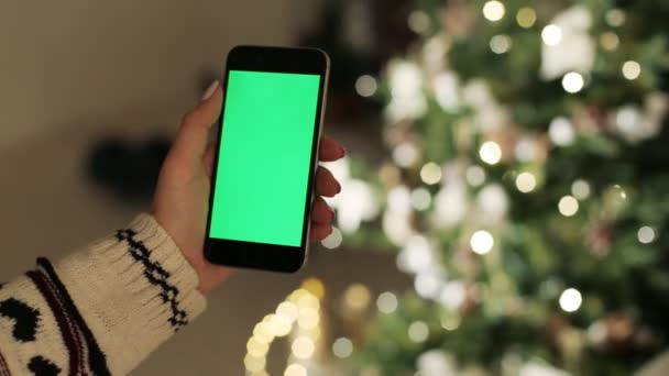 Közeli a nő kezét, megérintette a smartphone. Zöld képernyő Chroma Key. Közelről. Mozgás követés. a karácsonyi dekoráció háttér életlenítés — Stock videók