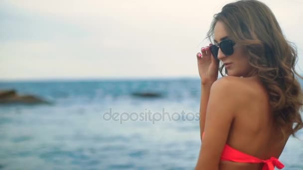 Close up van jonge aantrekkelijke model in zwarte zonnebril en rode badpak op het strand. — Stockvideo