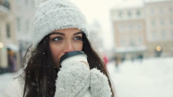 Felicidade, férias de inverno, Natal, bebidas e conceito de pessoas - sorrindo jovem mulher em roupas quentes brancas com e beber café para tirar sobre fundo da cidade nevado — Vídeo de Stock