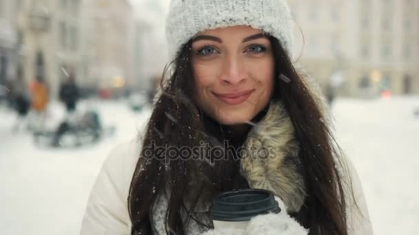 Felicidad, vacaciones de invierno, Navidad, bebidas y el concepto de la gente - Alegre hermosa morena en la moda de invierno sosteniendo taza desechable en el fondo urbano — Vídeos de Stock