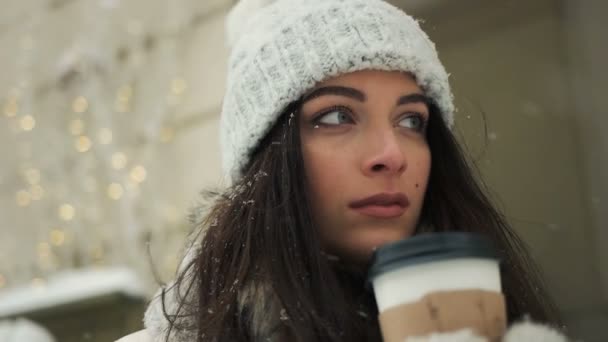 幸福、冬休み、クリスマス、飲料、人々 の概念 - 白暖かい服の若い女性の笑顔と奪う雪都市の背景の上にコーヒーを飲む — ストック動画