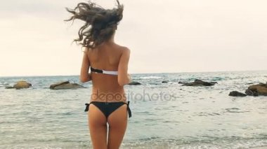 Siyah ve beyaz mayo bir plaj su üzerinde çalışan genç seksi kadın.