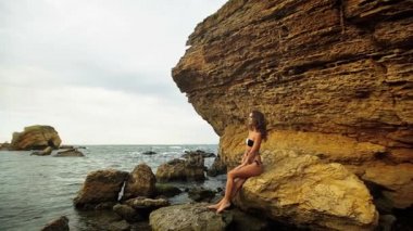 Bir taş üzerinde oturan ve güzel vücudu dokunmadan çekici genç bayan.