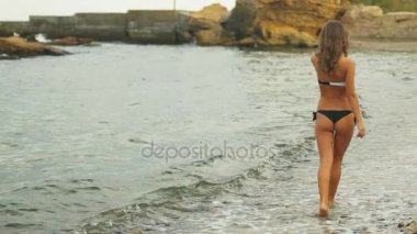 Güzel bir çöl plaj kum üzerinde yürüyen siyah ve beyaz bikinili seksi genç bayan.