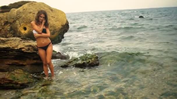 매력적인 맞는 검게 레이디 그녀의 휴가의 시간에서 돌 해변에는 카메라에 포즈. — 비디오