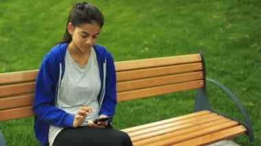 Smartphone ellerinde tutan bir bankta oturan genç güzel Bayan.