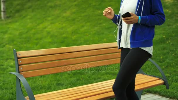 Feliz joven activa mujer relajándose en un banco después de los entrenamientos en un aire fresco . — Vídeo de stock