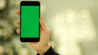 Yakın çekim yeşil ekran cep telefonunda dokunmadan eller. Mobil cihazlar yeşil ekranda. Chroma anahtar yeşil ekran. Yakın çekim. Hareket izleme. Vertical.with bulanıklık Noel dekorasyon