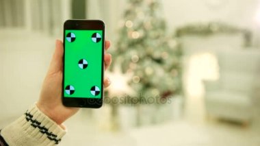 Yakın çekim yeşil ekran cep telefonunda dokunmadan eller. Chroma Key. Yakın çekim. Hareket izleme. Vertical.with Noel dekorasyon arka plan bulanıklık
