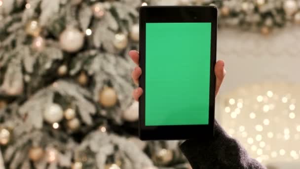 Közeli kép a női kéz a tabletta zöld zöld képernyő megérintésével képernyő Chroma Key. Közelről. Mozgás követés. Vertical.with karácsonyi dekoráció háttér életlenítés — Stock videók
