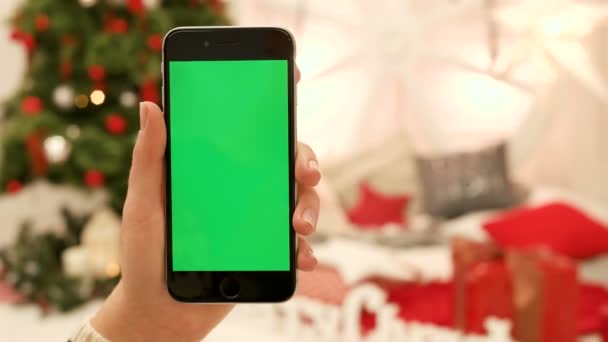 Gros plan des mains féminines touchant l'écran vert sur le téléphone mobile. Chroma Key. Ferme là. Suivi du mouvement. Vertical.with flou fond de décoration de Noël — Video