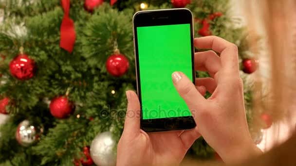 Primer plano de las manos femeninas tocando la pantalla verde en el teléfono móvil. Chroma Key. De cerca. Movimiento de rastreo. Vertical.with difuminación Navidad decoración fondo — Vídeo de stock