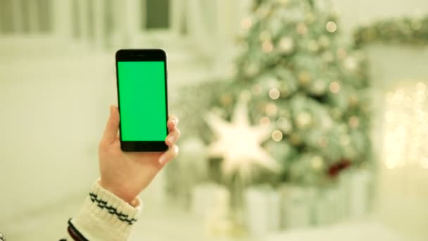 携帯電話でグリーン スクリーンに触れる女性の手のクローズ アップ。クロマ キー。クローズ アップ。モーションをトラッキングします。Vertical.with は、クリスマスの装飾背景をぼかし — ストック動画