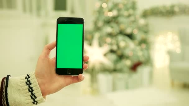 Gros plan des mains féminines touchant l'écran vert sur le téléphone mobile. Chroma Key. Ferme là. Suivi du mouvement. Vertical.with flou fond de décoration de Noël — Video
