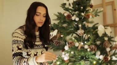 Bir Noel ağacı oyuncaklar koyarak sıcak kazak giyen genç güzel kadın.