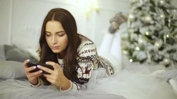 Όμορφη κοπέλα σε ένα κομψό πουλόβερ και χαριτωμένο κάλτσες, χρησιμοποιώντας το κινητό σπίτι σε ένα διακοσμημένο δωμάτιο. — Αρχείο Βίντεο