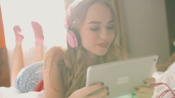 Belle jeune femme dans les écouteurs regarder des vidéos drôles dans sa tablette . — Video