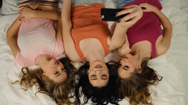 Sorrindo jovens senhoras tomando selfies enquanto deitado na cama após grande festa de pijama . — Vídeo de Stock