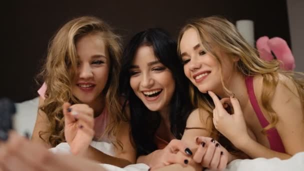 Τρεις όμορφες χαμογελώντας σγουρά φίλους με παρόμοιες καρφιά για τη λήψη selfie στο κρεβάτι. — Αρχείο Βίντεο