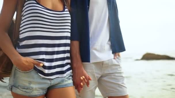 Close up of two young people holding hands and walking on the beautiful beach. — Stock Video