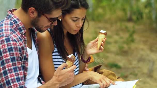 Two young tourist sitting on the bench, holding map on hands and eating tasty ice-cream. — Stock Video