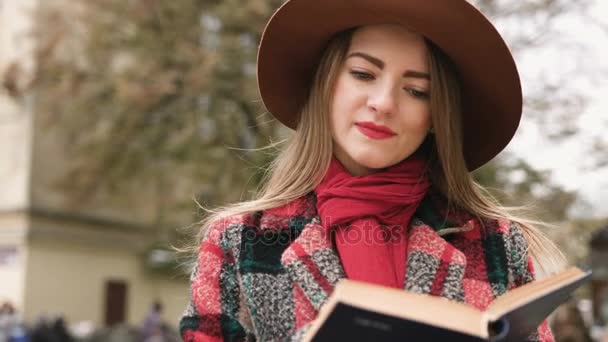Ung vacker flicka i hatt läsa bok i stadsparken. Slow motion. — Stockvideo