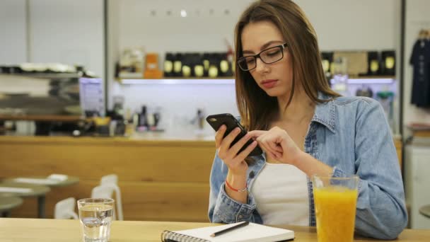 Mladá krásná žena, psaní na smartphone, surfování na internetu a pití šťávy v kavárně — Stock video