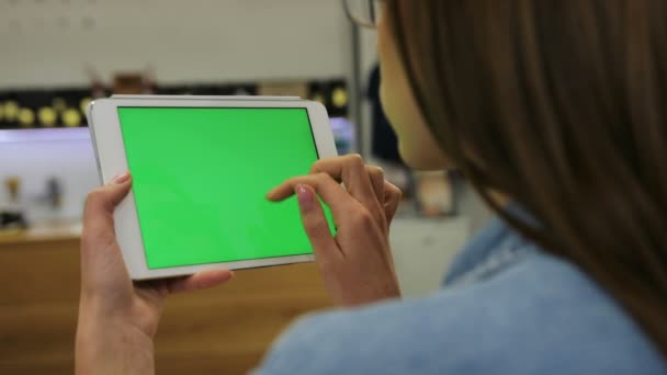 Junge attraktive Frau mit Tablet mit grünem Bildschirm sitzt im Café, wischt Bilder, Nachrichten. Nahaufnahme. Chroma-Schlüssel — Stockvideo