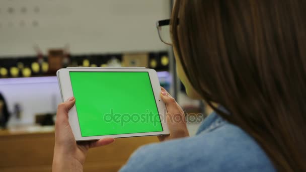 Jovem mulher atraente em óculos assistindo vídeo em tablet com tela verde no café. Close-up. Chave Chroma. Creme verde — Vídeo de Stock