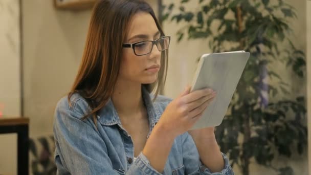 Привлекательная молодая женщина в очках и голубой рубашке с помощью планшетного компьютера в кафе, вид через окно — стоковое видео