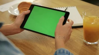 Kadının Close-Up tablet kafede yeşil ekran ile sayfa aşağı kaydırma eller. Yakın çekim. Chroma anahtar. Yeşil ekran. sosyal ağ