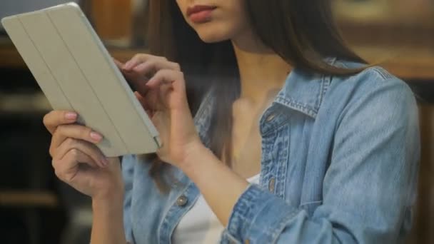 Sluit video van mooie jonge vrouw met behulp van tablet pc in het café, kijk door het raam. Te tikken en te scrollen. — Stockvideo