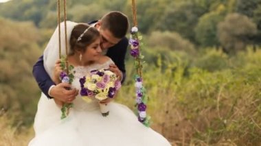Öpüşme damat ve güzel gelini beyaz gelinlikle çiçek kokulu yaz ormandaki salıncak üzerinde sallanan, park