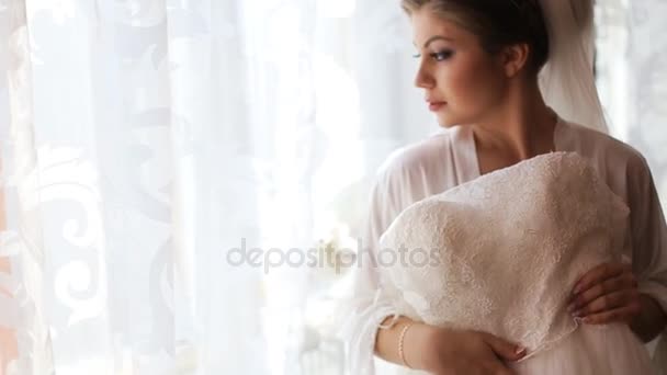 Όμορφη νύφη προσπαθεί με κορδόνια νυφικό πριν από τη γαμήλια τελετή και ψάχνει μέσα από το παράθυρο — Αρχείο Βίντεο